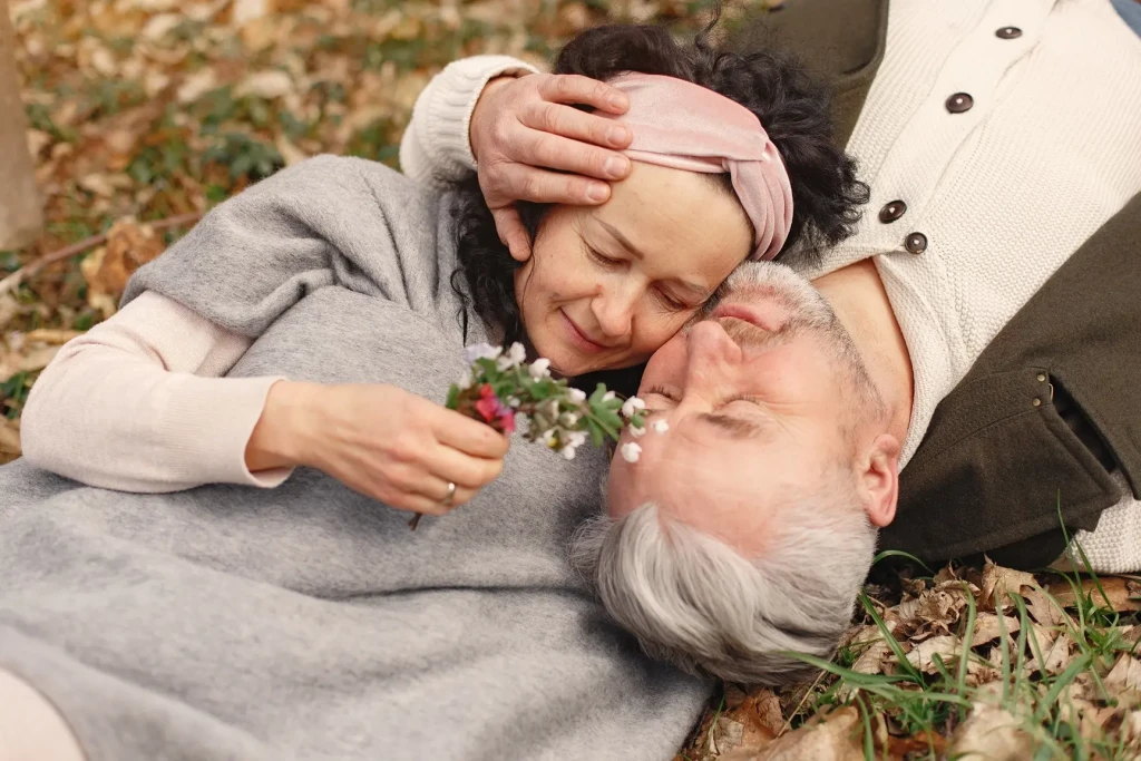 Couple de seniors allongés dans l’herbe au printemps partageant un moment tendre en pleine nature