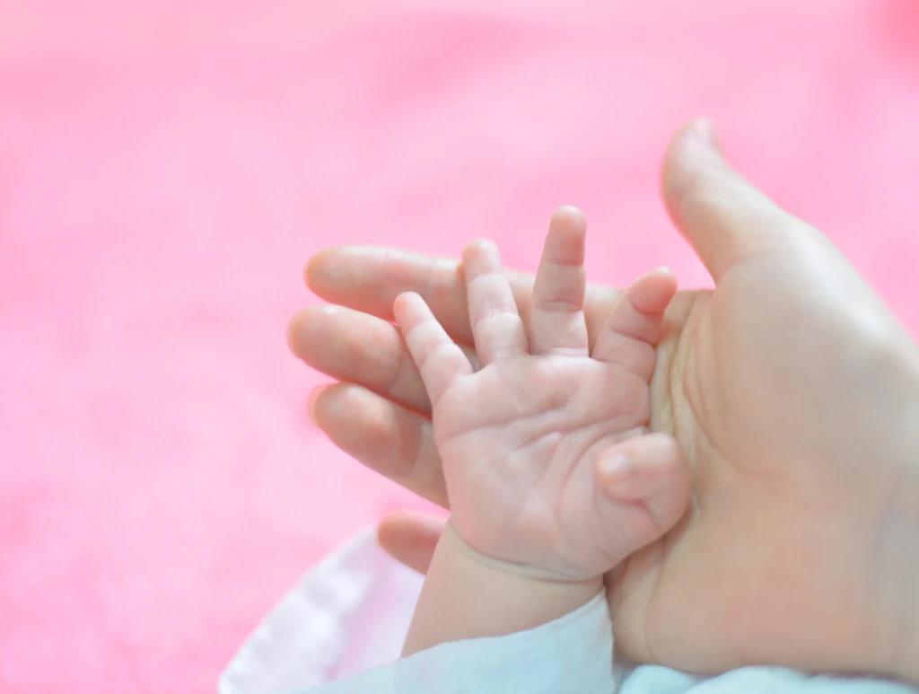 Main de bébé tenant le doigt d’un parent sur fond rose