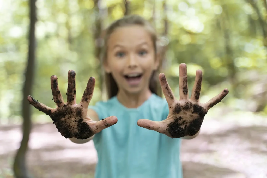 Enfant souriant montrant ses mains couvertes de terre après une activité en plein air en forêt
