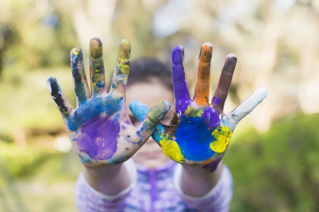 Enfant montrant ses mains couvertes de peinture colorée lors d’une activité créative en extérieur