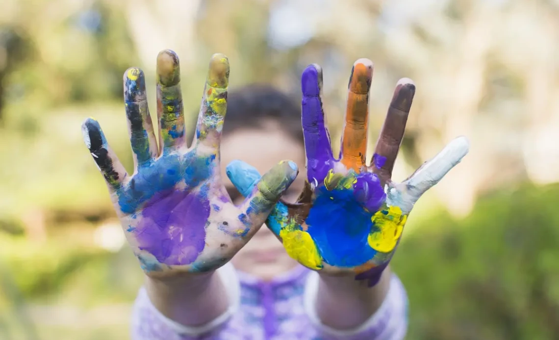 Enfant montrant ses mains couvertes de peinture colorée lors d’une activité créative en extérieur